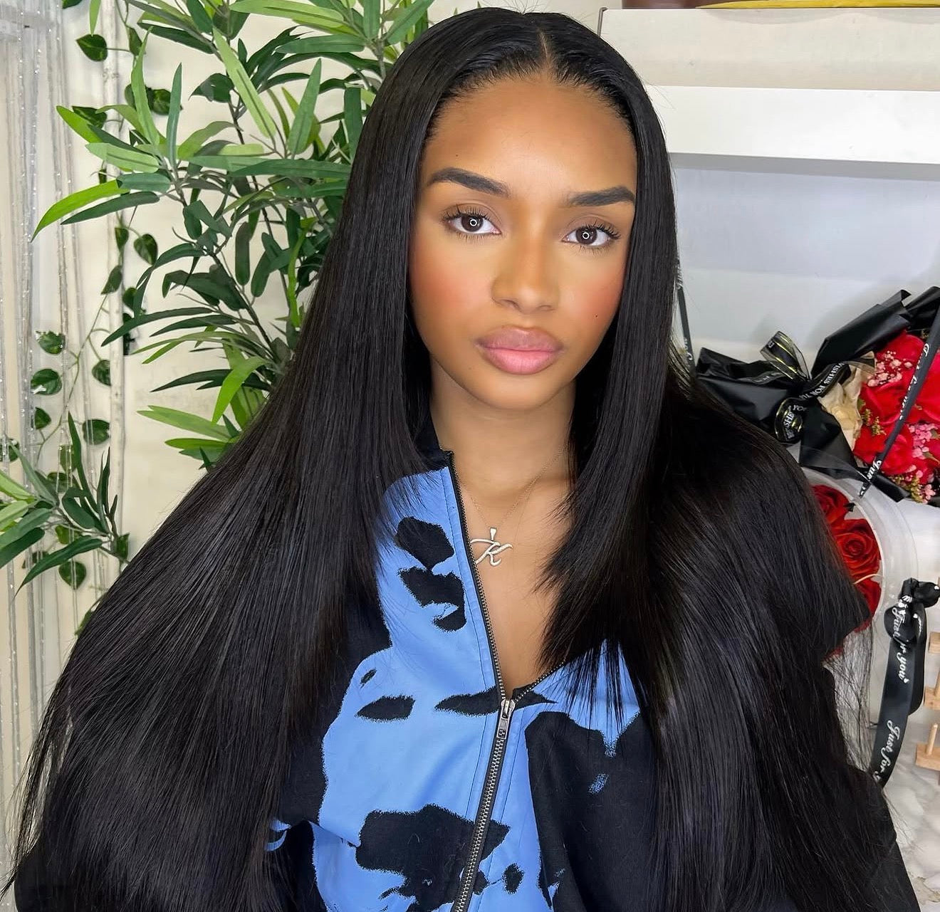 Woman with long black hair wearing a blue and black patterned jacket indoors.